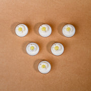 Six white flower tealight candles arranged in a triangle on a brown surface